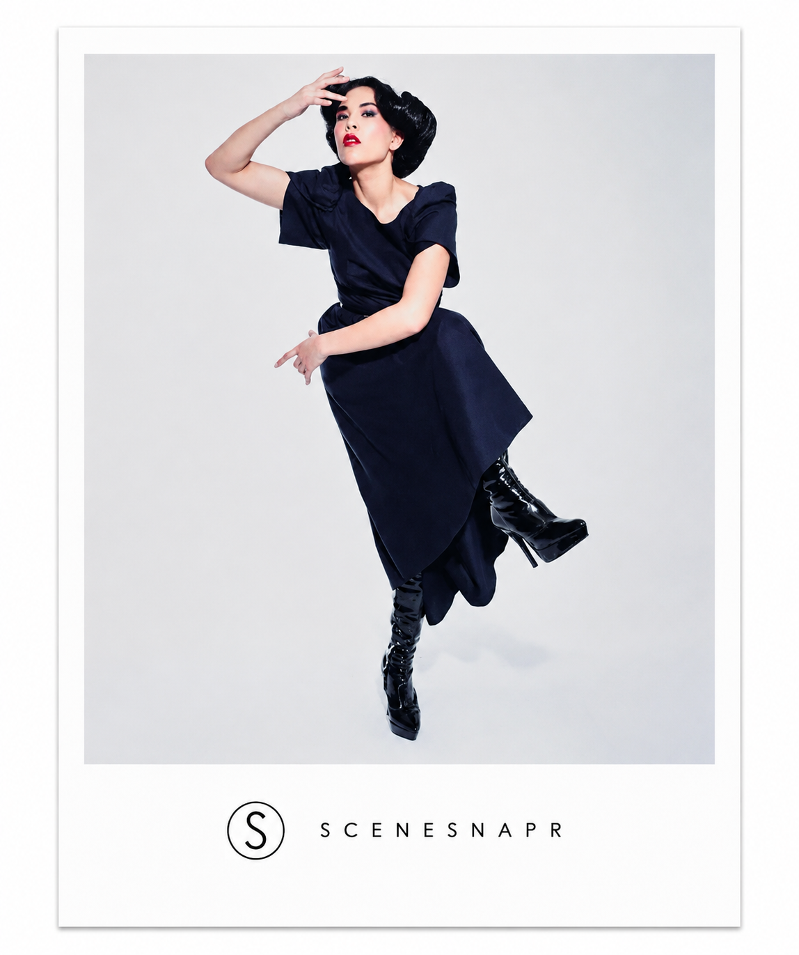 Editorial fashion styling: studio image of a model in a dark draped dress and patent boots